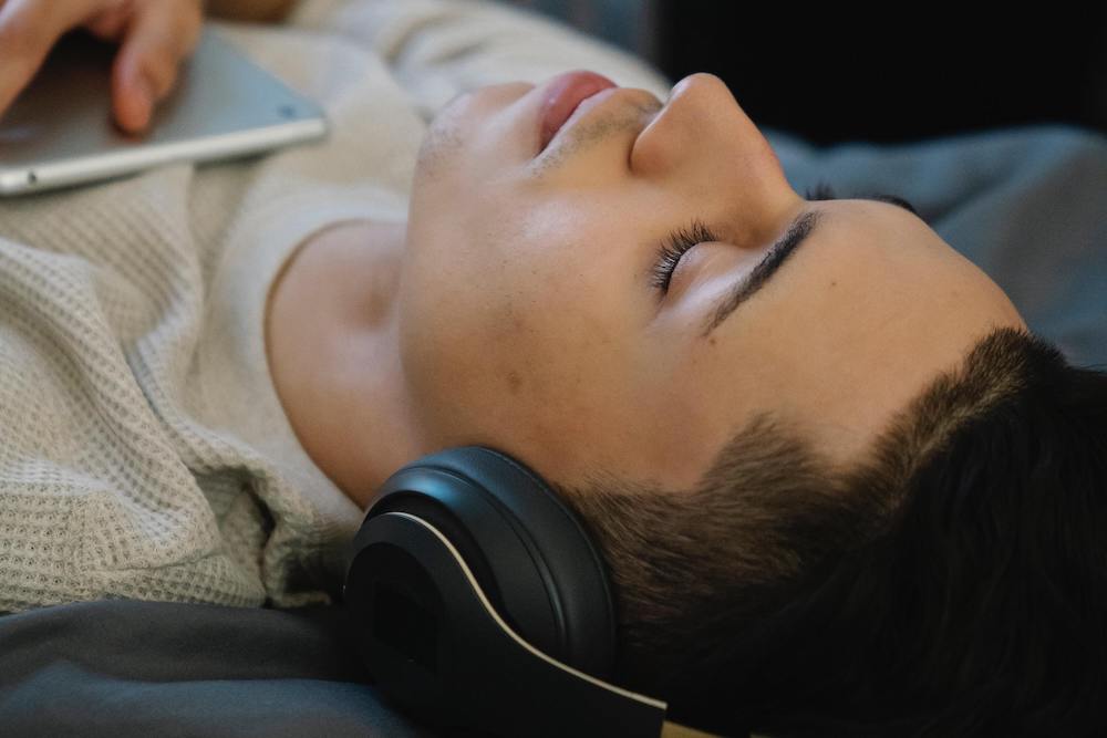 Young man lying down wearing headphones and listening to binaural beats