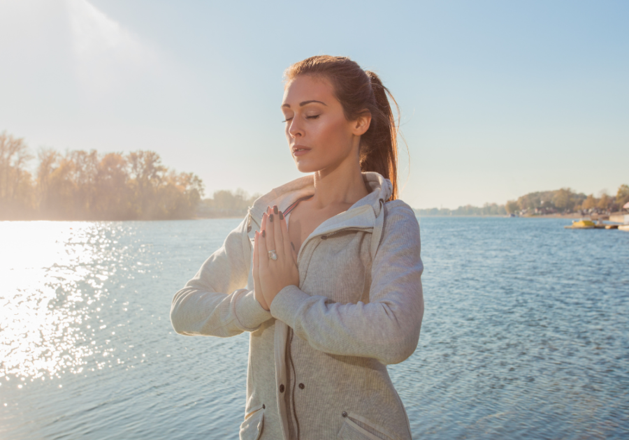 woman with hands in prayer position standing near the sea affirmations for peace